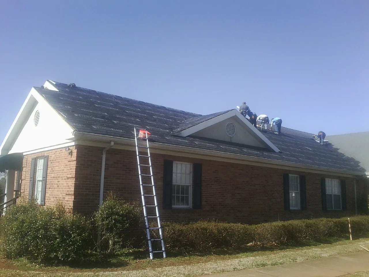 Crew tearing shingles off a brick ranch roof with a ladder set — Emergency Roof Repair work by our crew in Crab Orchard